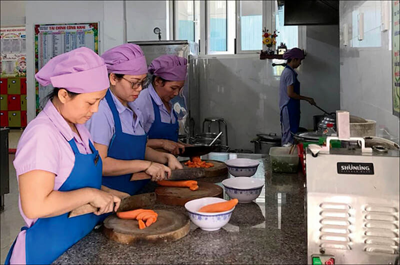 Đồng phục nhà bếp cấp dưỡng màu tím nhạt với tạp dề xanh nhã nhặn